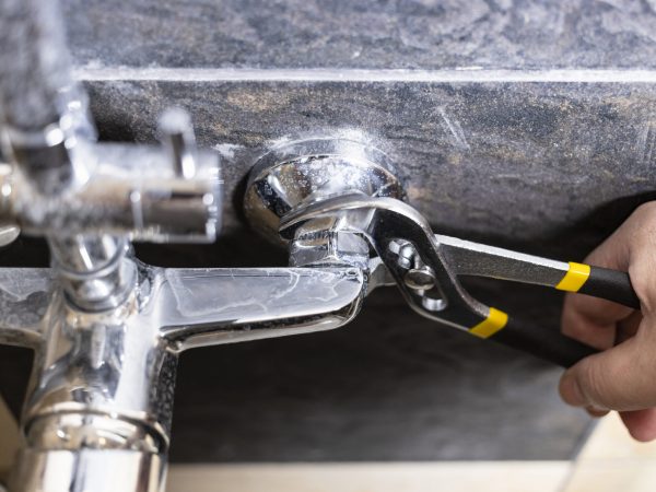 plumber unscrews nut of shower faucet close up on tiled wall at home